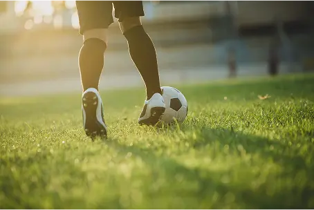 Uma vista aproximada de um jogador de futebol a mover a bola pelo campo, destacando treino, técnica e prática de futebol ao ar livre.